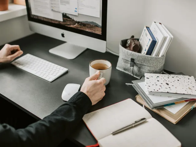 Tidy bookkeeping desk with laptop, coffee and notebook — monthly accounting cadence in motion.